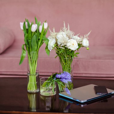 Cep telefonu ve laptop yakınındaki bir masada zarif basit Vazolar Çiçek demetleri. İş yerinde çiçekçi dekoratör, bir yaşam tarzı