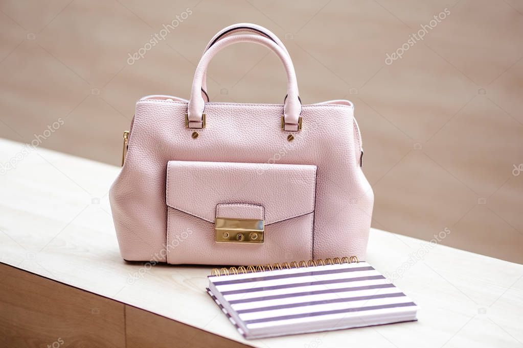 Close-up photo of modern light pink handbag near notebook planner