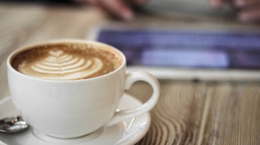 Genç kadın bir arka plan üzerinde ahşap bir masa üzerinde kahve dijital tablet ile çalışır