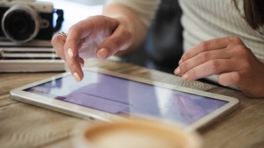 Genç kadın kahve ahşap bir masa üzerinde bir arka plan üzerinde dijital tablet ile çalışıyor