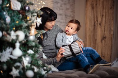 Rahat bir ceket ve kot pantolon onun büyükannesi ile Noel ağacının yanında oturan küçük oğlu 