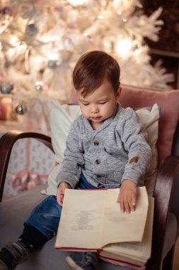 Rahat bir ceket ve kot hediyelerle yılbaşı ağacının yanında oturan küçük oğlu