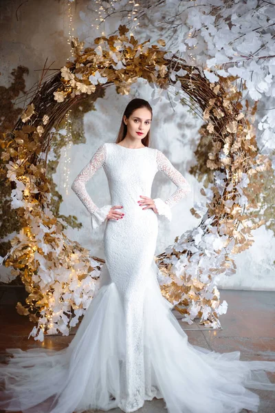 Fashion portrait of beautiful young woman in a gorgeous wedding dress, posing in a fantasy interior with white winter tree