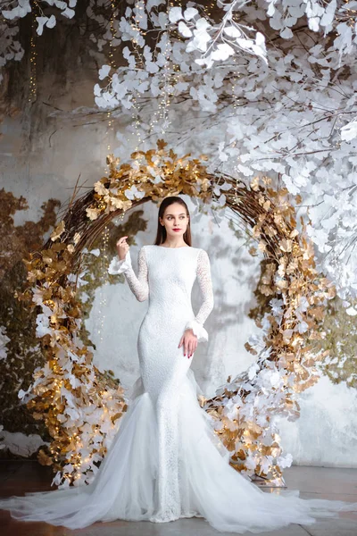 Fashion portrait of beautiful young woman in a gorgeous wedding dress, posing in a fantasy interior with white winter tree