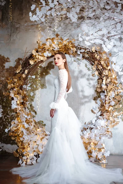 Fashion portrait of beautiful young woman in a gorgeous wedding dress, posing in a fantasy interior with white winter tree