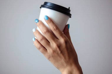 Güzel manikür, pastel ihale mavi renk oje, closeup fotoğraf. Eller bir plastik kahve fincanı basit arka plan üzerinde tutun. 