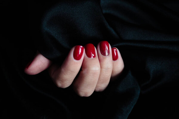 Великолепный маникюр, лак для ногтей красного цвета, красивая фотография. Женские руки на темном фоне меха
 