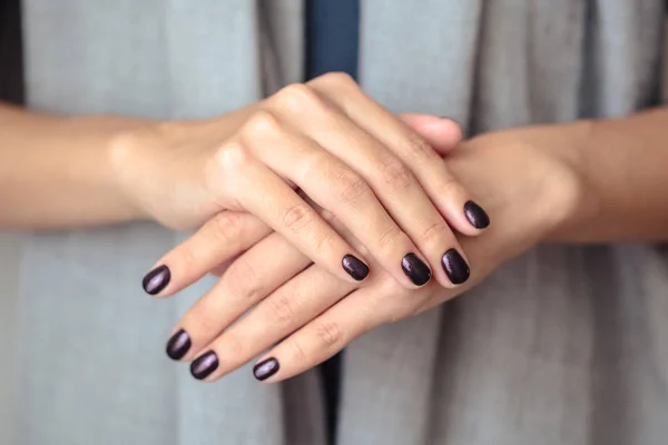 Gorgeous manicure, dark purple tender color nail polish, closeup photo. Female hands over simple background of casual clothes