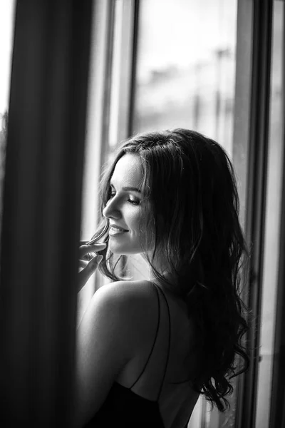 Black white portrait of young woman in elegant silk black dress lookingto a city from a balcony, fashion beauty photo