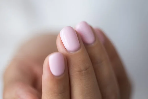 Close-up photo of elegant light pink manicure over white shirt background, tender women\'s hands with perfect nails, spa and care