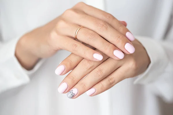 Close-up photo of elegant light pink manicure over white shirt background, tender women\'s hands with perfect nails, spa and care