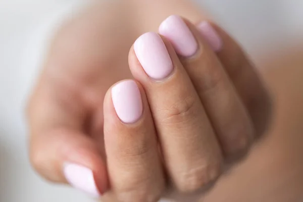 Close-up photo of elegant light pink manicure over white shirt background, tender women\'s hands with perfect nails, spa and care