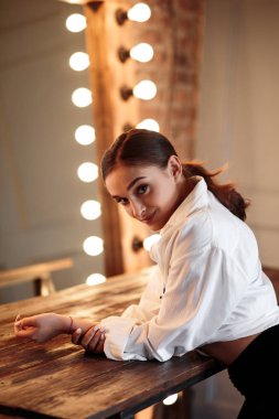 Genç esmer kadın büyük ayna yakınında poz. Mükemmel makyaj ve şık at kuyruğu, erkeksi stil, ince şekil