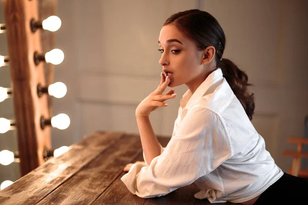 Young brunette woman posing near big mirror. Perfect makeup and stylish ponytail, masculine style, slim figure