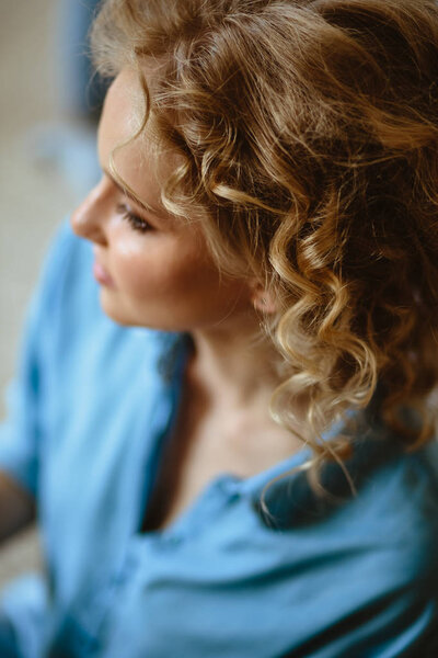 Pretty cheerful blonde young woman with curly hair and charming smile resting in her home, room with modern scandinavian interior