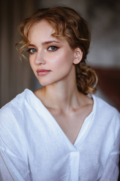 Young blonde woman in a casual white shirt and jeans in a loft interior, close up fashion portrait