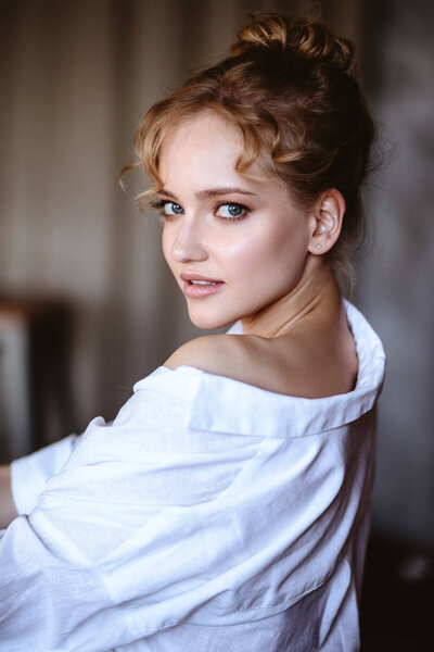 Young blonde woman in a casual white shirt and jeans in a loft interior, close up fashion portrait