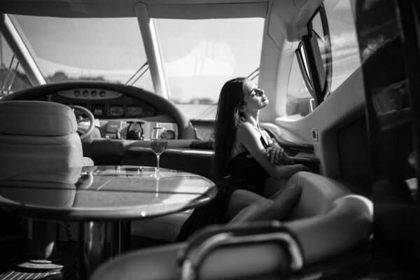 Young beautiful woman in a long silk black dress posing on a yacht. Luxurious life style, summer time
