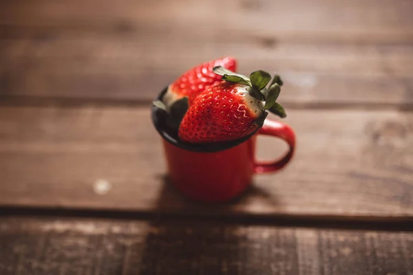 several strawberries in a red enamel mug on a wooden table