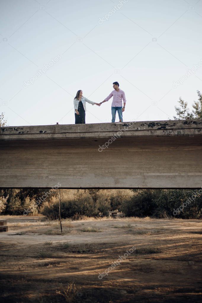 young couple in love holding hands on an old bridge at sunset