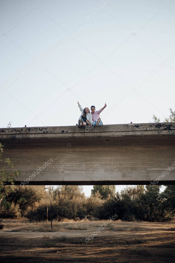 young couple in love raising their hands on an old bridge at sunset