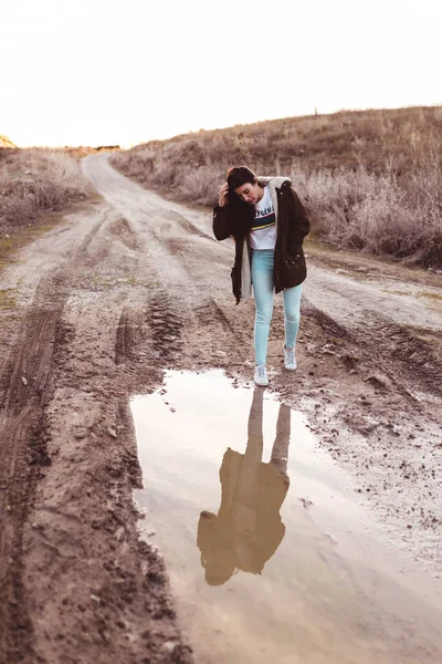 young woman looking in the puddle at sunset in the countryside