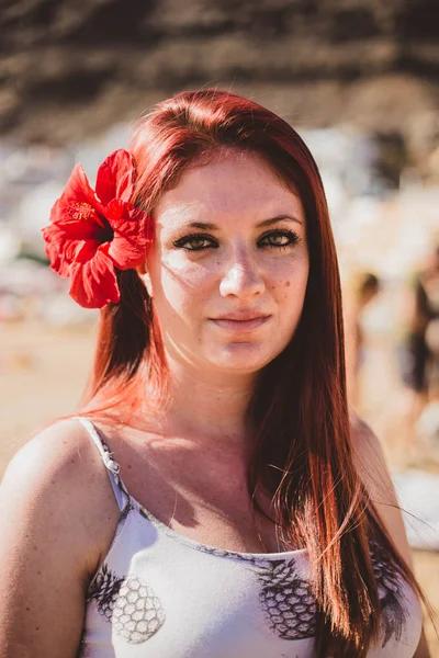 Bonita joven pelirroja en la playa con una gran flor roja en el pelo — Foto de Stock