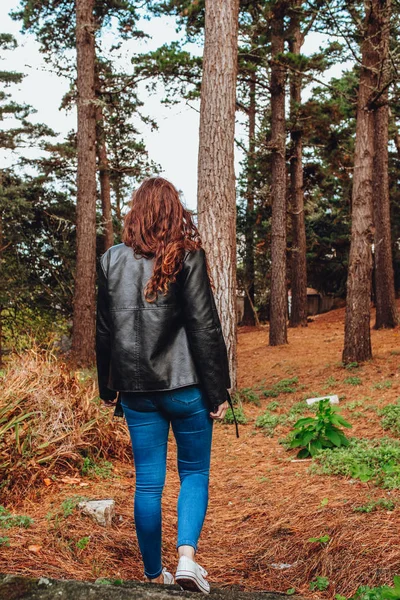 Mujer joven con pelo rizado y chaqueta negra caminando por el bosque — Foto de Stock