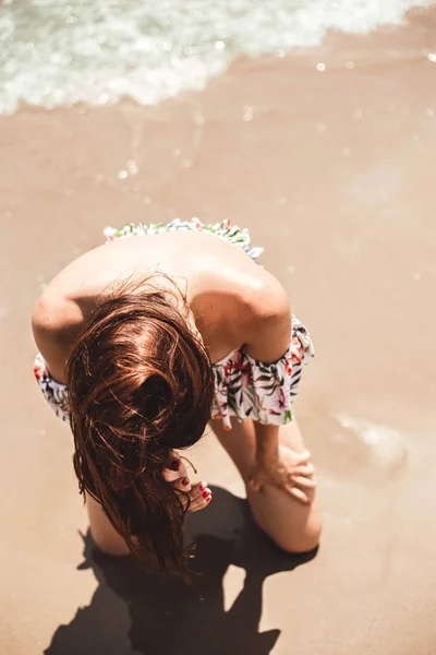Hermosa joven arrodillada en la orilla del mar moviendo su pelo brillante — Foto de Stock