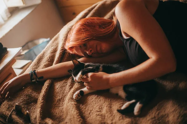 Руда жінка лежить на ліжку погладжуючи кошеня — стокове фото