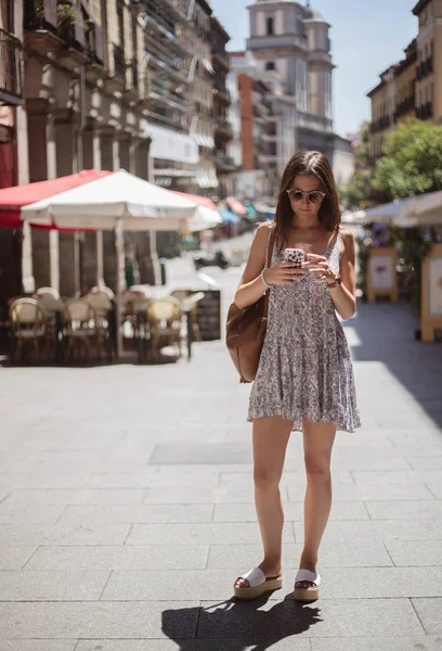 ผู้หญิงสาวเดินและใช้สมาร์ทโฟนในถนนนักท่องเที่ยวในวันฤดูร้อนในมาดริด — ภาพถ่ายสต็อก