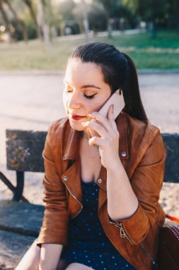 Gözleri kapalı genç bir kadın bir bankta oturan akıllı telefondan konuşuyor ve dinliyor.
