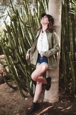 model kaktüs yakınındaki bir ağacın gövdesi üzerinde istirahat siyah kapak ile gülüyor