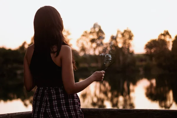 Donna bruna al tramonto su un lago con un bastoncino di incenso — Foto Stock