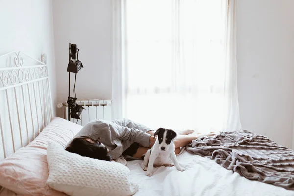 Young sad brunette woman caressing her labrador puppy lying in bedroom — ストック写真