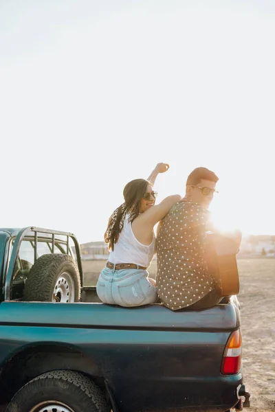 Jóvenes amantes de los viajeros se divierten con la guitarra en la parte superior del coche jeep 4x4. Pareja que hace un wanderlust vacaciones en la puesta del sol en verano —  Fotos de Stock