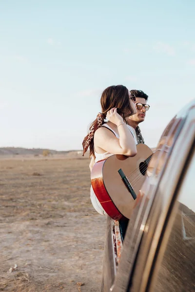 Νέοι ταξιδιώτες λάτρεις της διασκέδασης με την κιθάρα στην κορυφή του τζιπ 4x4 αυτοκίνητο. Ζευγάρι κάνει μια καλή διακοπές το καλοκαίρι — Φωτογραφία Αρχείου