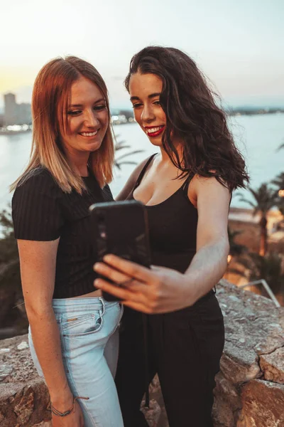 Két nő barátai vesz egy selfie a strand közelében a meleg fényében a naplemente este — Stock Fotó