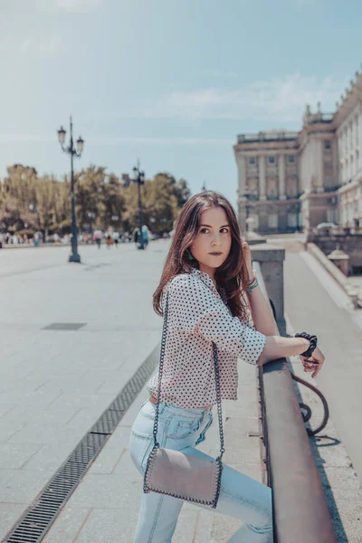 ผู้หญิงสาวที่สวยงามพร้อมกระเป๋าถือ พักอยู่บนรั้วใกล้พระราชวังแห่งมาดริด สเปน — ภาพถ่ายสต็อก