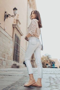 Kahve kahverengi saçlı genç kadının tam uzunlukta arka arka. Sokakta poz veren model.