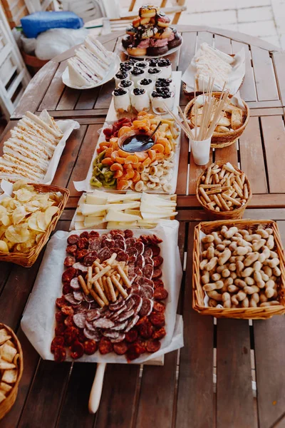 Closeup de tábua de corte com chouriço, salame, queijo, batatas fritas, pão, sanduíches, rosquinhas, iogurte, frutas fondue tangerina, banana, kiwi, mirtilos, morangos em uma mesa de madeira . — Fotografia de Stock