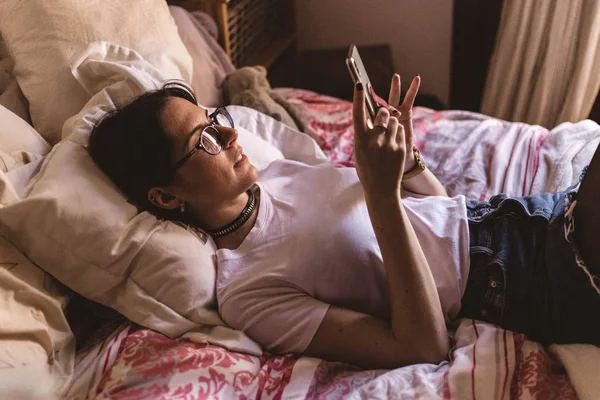 สาวสวยยิ้มกับแว่นนอนบนเตียงและพิมพ์ — ภาพถ่ายสต็อก