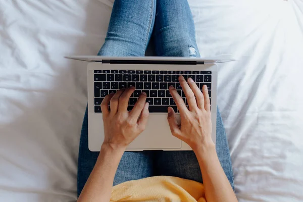Невідома жінка сидить на ліжку, друкуючи на ноутбуці — стокове фото