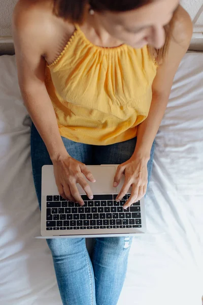 Femme méconnaissable assise sur le lit tapant sur l'ordinateur portable Images De Stock Libres De Droits