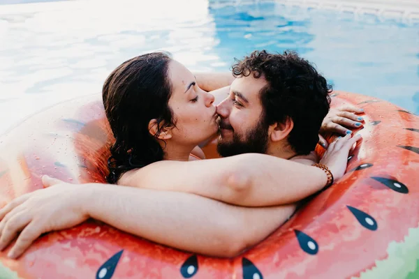 Pareja joven en sandía inflable en piscina en el hotel. La mujer besa la nariz de su novio. Vacaciones de verano, estilo de vida. Momento de amor . —  Fotos de Stock