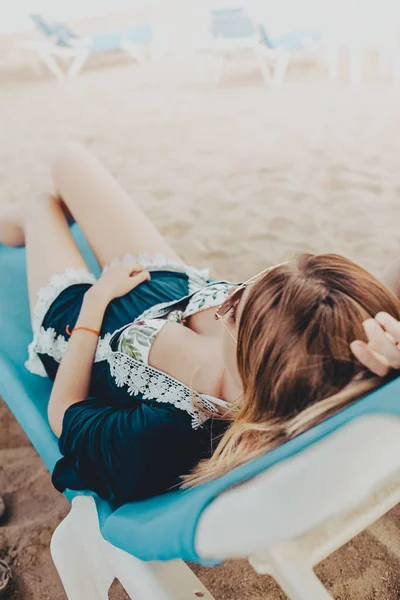 Giovane donna bionda con i capelli corti sdraiata su un'amaca blu con occhiali da sole che si gode la spiaggia — Foto Stock