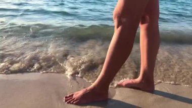 Deniz kıyısında yürüyen genç bir kadının bacakları