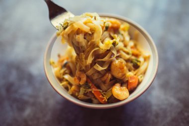 El koyu arka plan üzerinde sebze ve karides ile lezzetli erişte pikap için çatal kullanır. Asya gıda konsepti. Üstte görüntü.