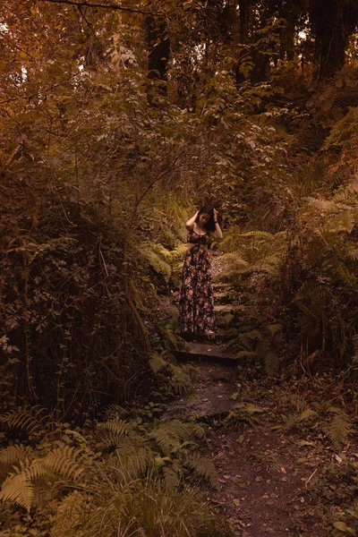 Mujer tierna en un vestido vintage negro tocando su cabello contra el fondo de la naturaleza ardiente otoño. Fotografía artística. Mujer en vestido sobre fondo de follaje de otoño . — Foto de Stock