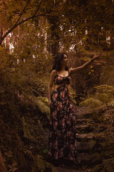 Eine zarte Frau in einem schwarzen Vintage-Kleid berührt Blätter vor dem Hintergrund feuriger Herbstnatur. künstlerische Fotografie. Frau im Kleid vor dem Hintergrund von Herbstlaub. — Stockfoto